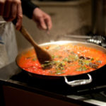 Motion blur photograph of chef stirring pasta sauce on stove.
