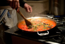 Motion blur photograph of chef stirring pasta sauce on stove.